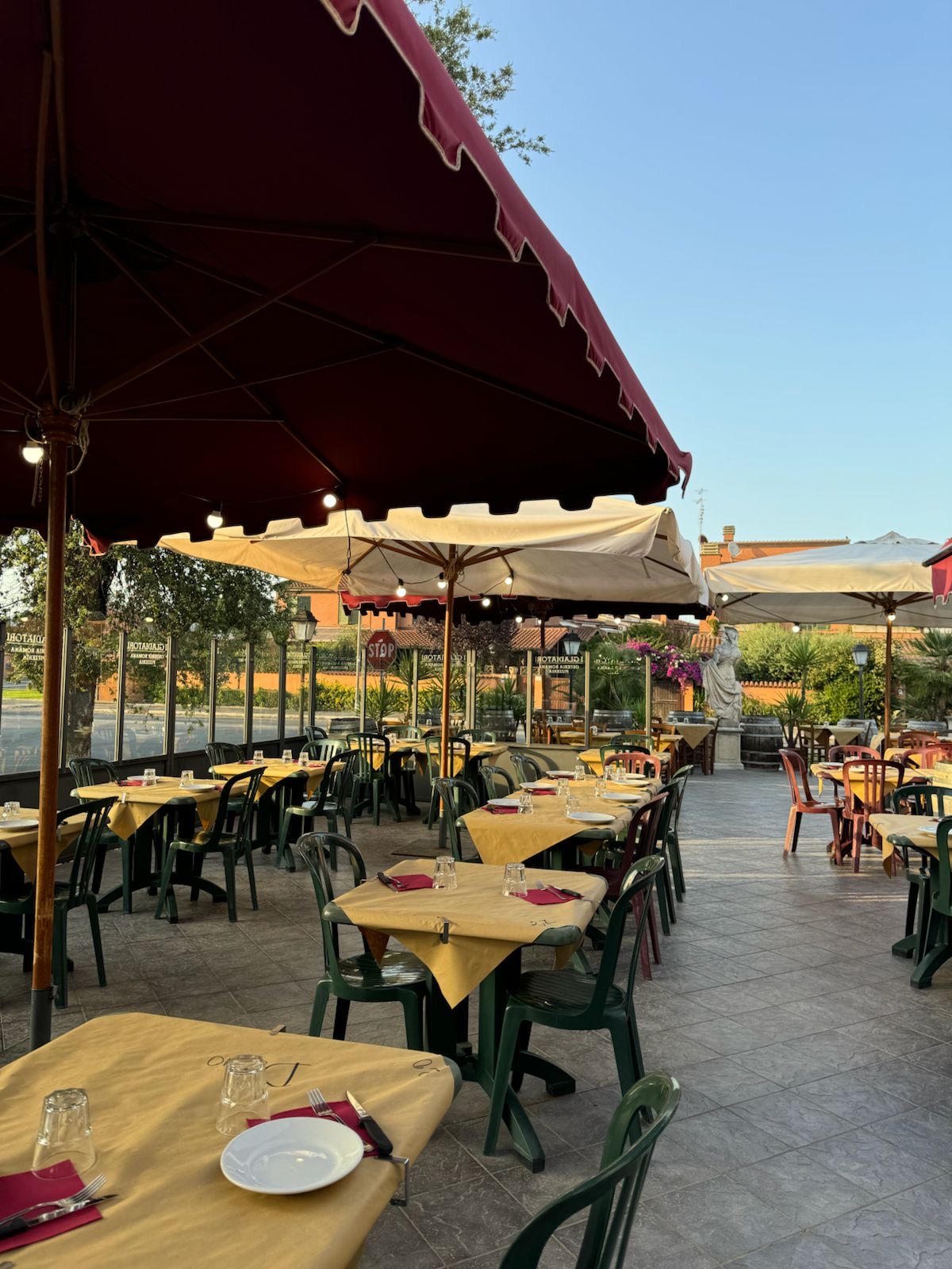 La terrazza esterna de I Gladiatori al tramonto, con ombrelloni bordeaux e tavoli apparecchiati